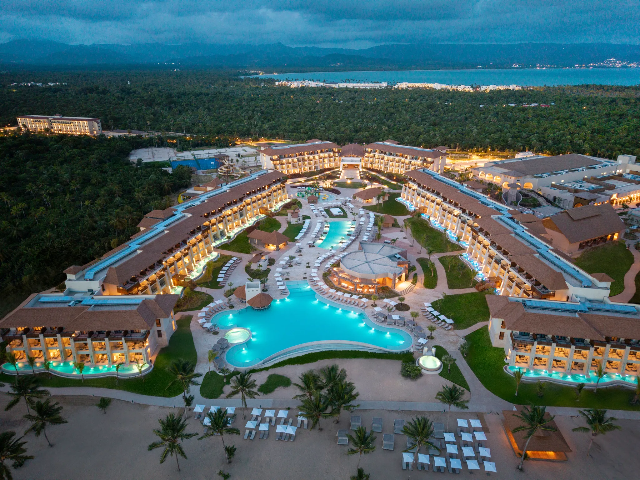 Sunrise aerial view of Dreams Playa Esmeralda Resort & Spa with illuminated pools and beachfront accommodations.
